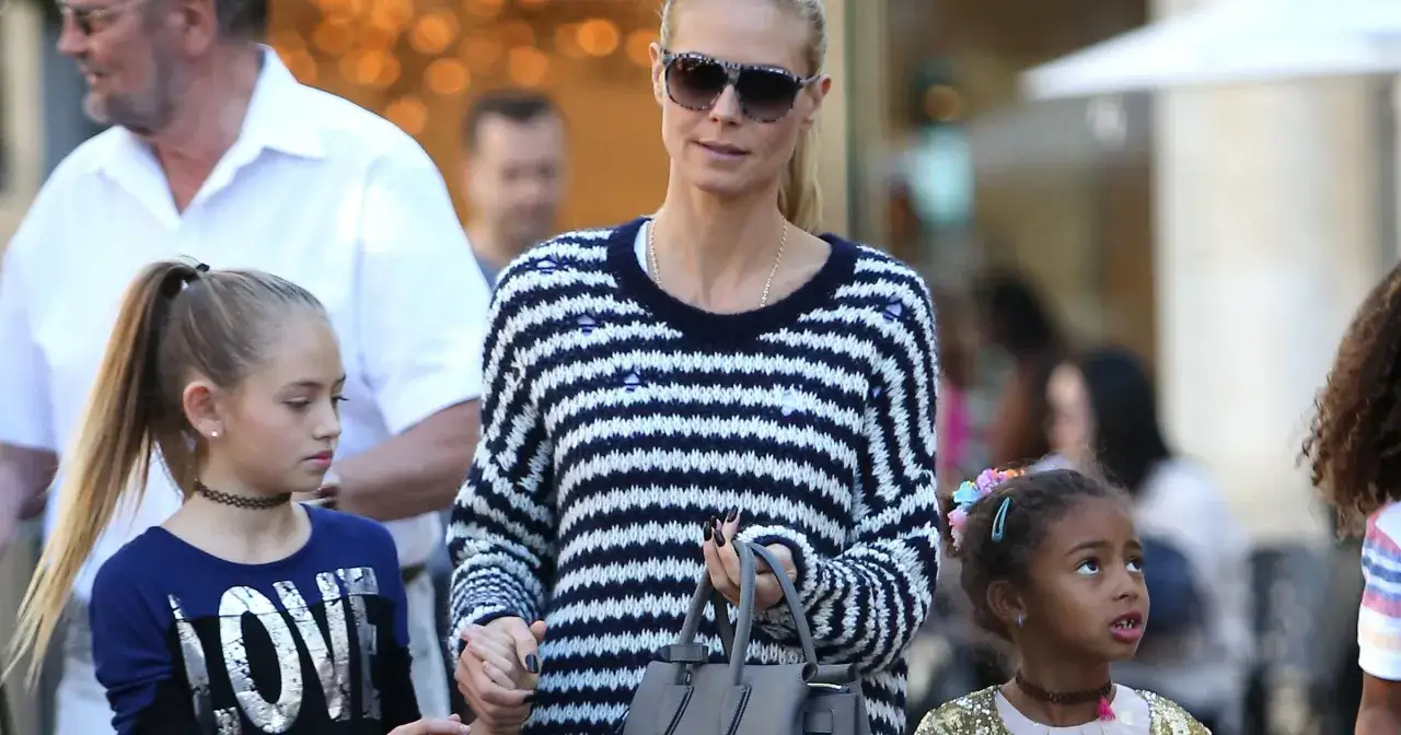 Heidi Klum z dziećmi spaceruje ulicą. Dwie dziewczynki, jedna z kucykiem, druga z kolorowymi spinkami we włosach, idą obok niej.