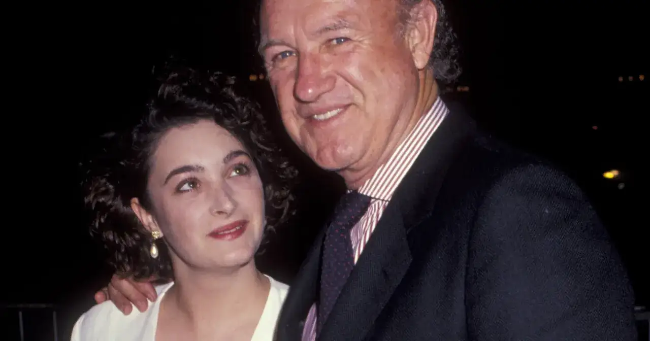 Gene Hackman z córką. Uśmiechnięty aktor w garniturze i elegancka kobieta z perłową kolczykiem.