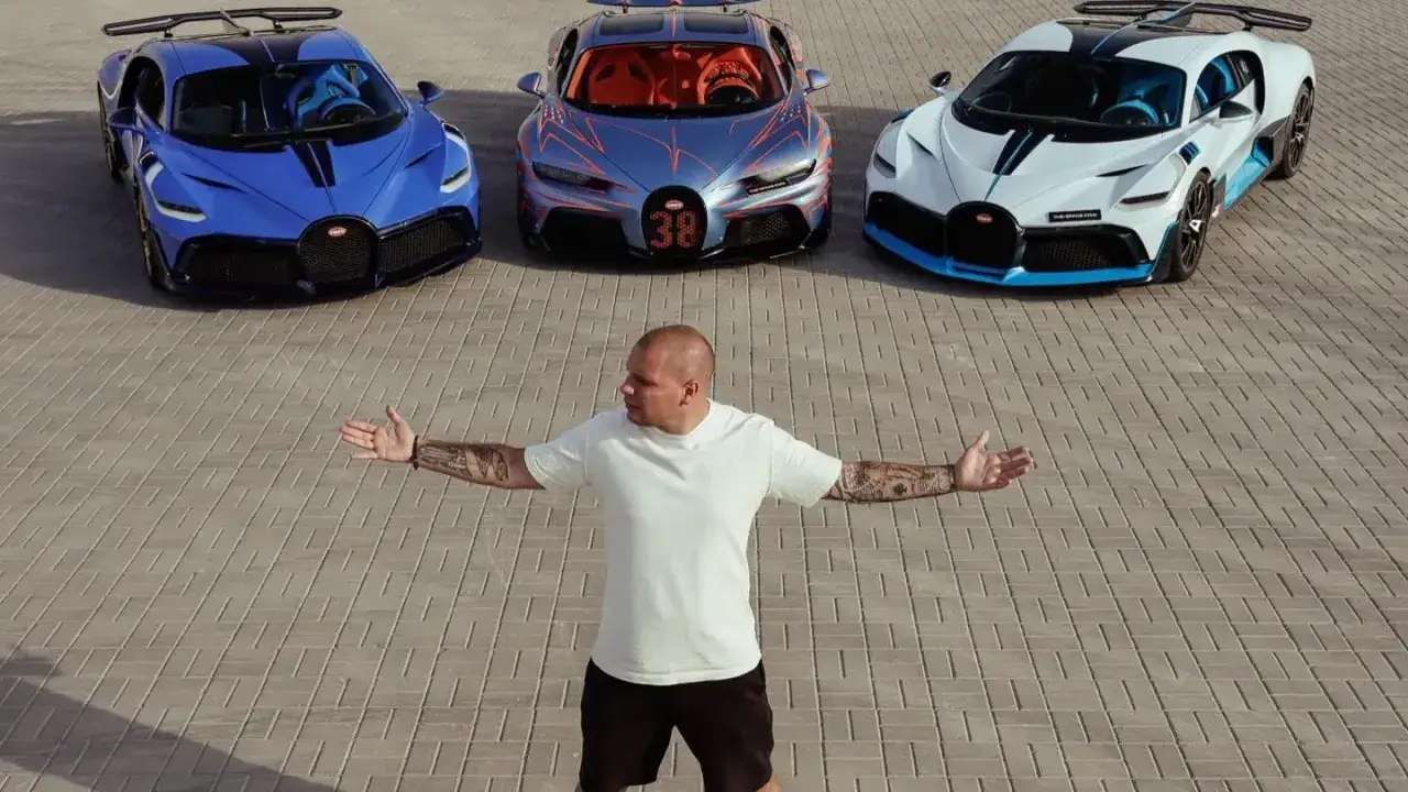 Mężczyzna w białej koszulce stoi przed trzema Bugatti: niebieskim, szarym i białym.