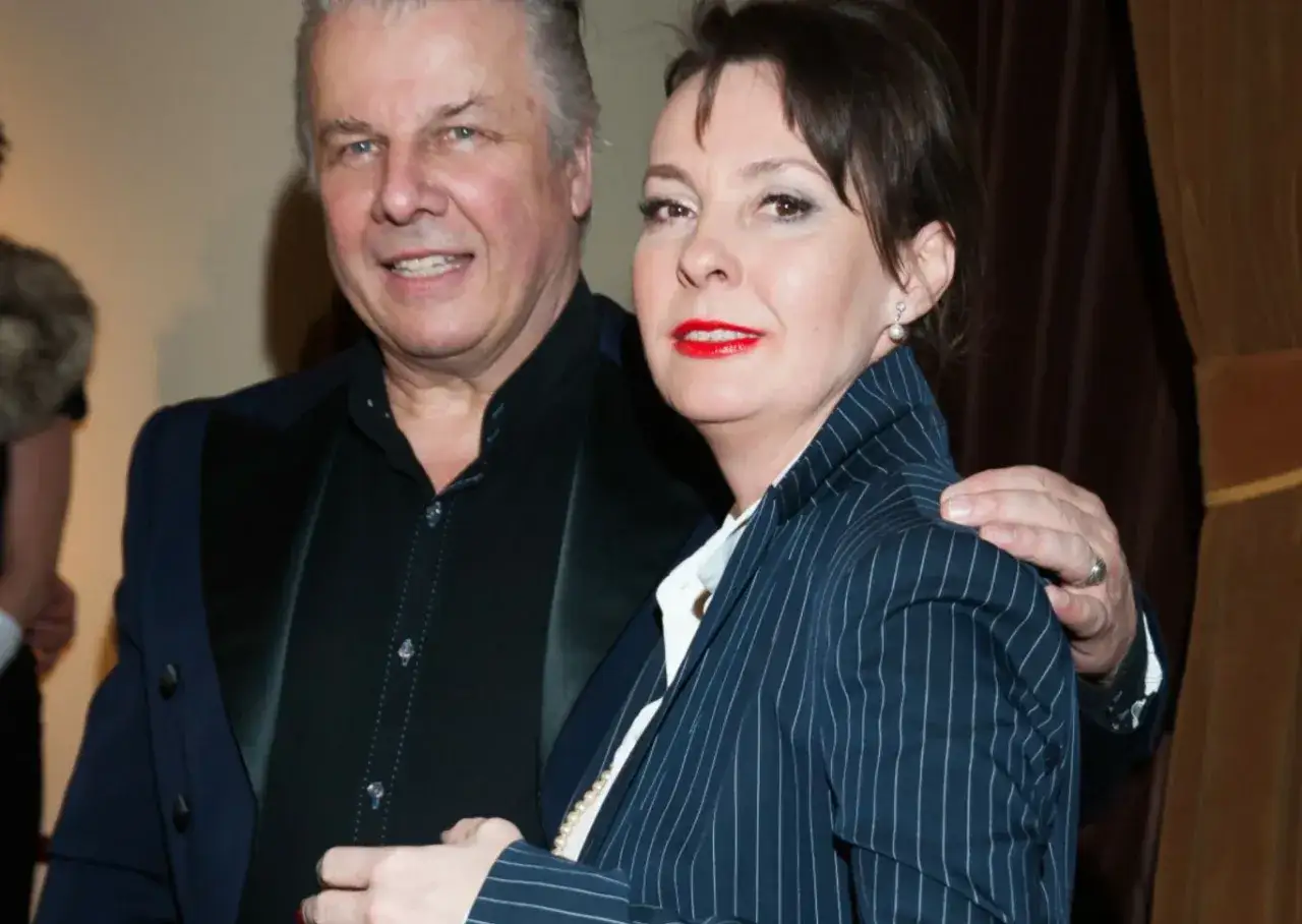 Izabella Jarska z mężem, uśmiechnięci, pozują do zdjęcia. Ona w granatowej marynarce w paski, on w czarnej koszuli i granatowej marynarce.