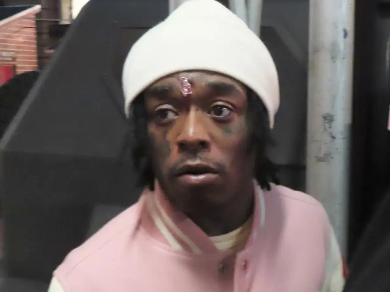 Lil Uzi Vert z różowym diamentem na czole, w białej czapce i kurtce.