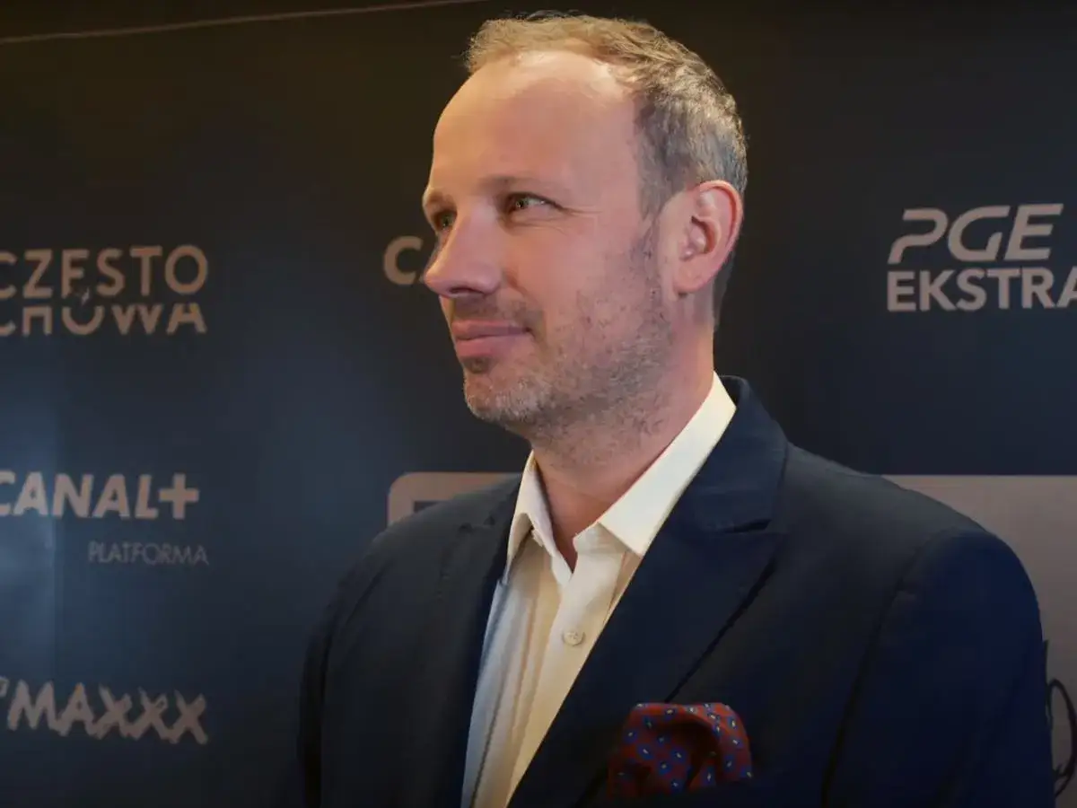 Marcin Majewski z TVN w eleganckim garniturze, uśmiecha się na tle logo PGE Ekstraklasy.
