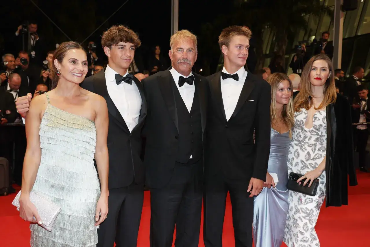 Kevin Costner z rodziną na czerwonym dywanie. Widać jego dzieci, synów i córkę, wszyscy elegancko ubrani.