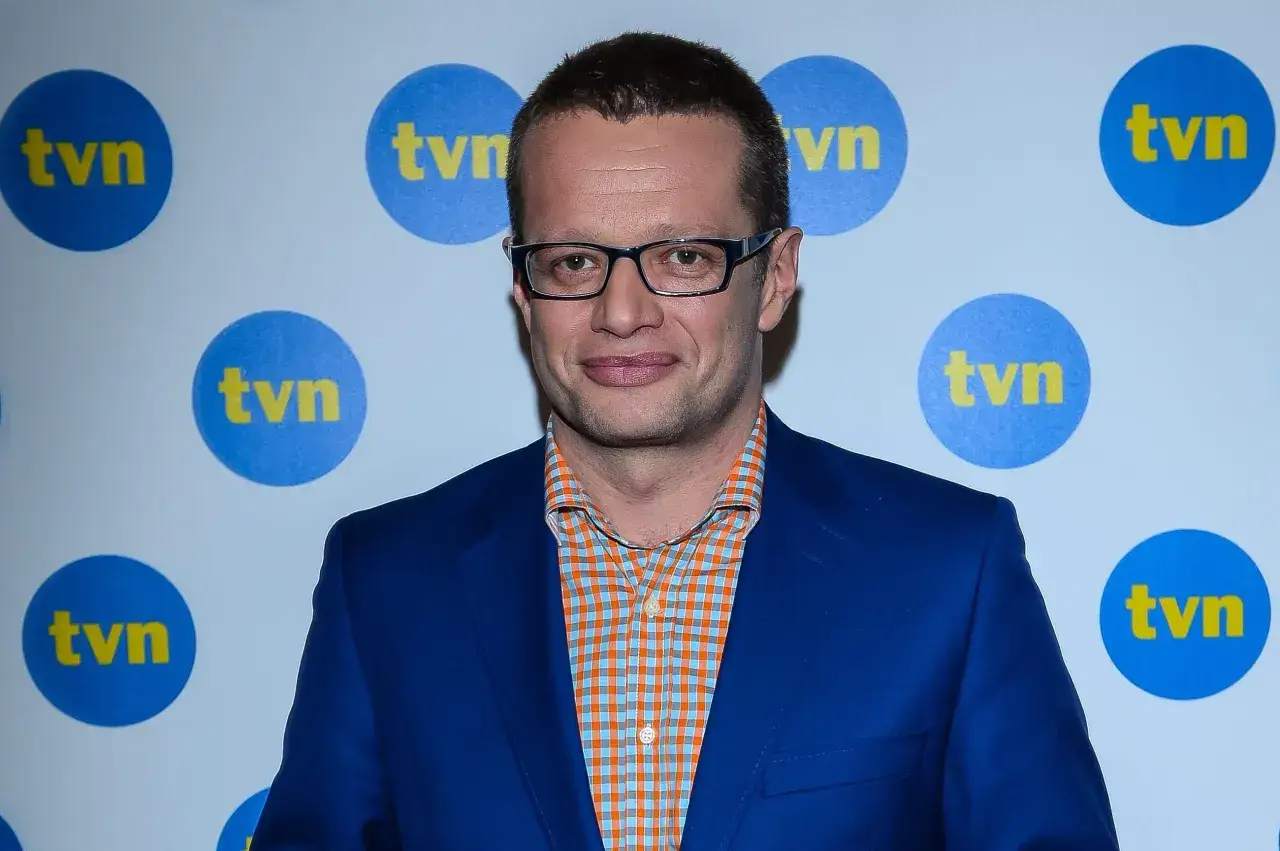 Mężczyzna w okularach i niebieskiej marynarce, na tle logo TVN. Wśród dziennikarzy i prezenterów TVN, ten pan wyróżnia się stylem.