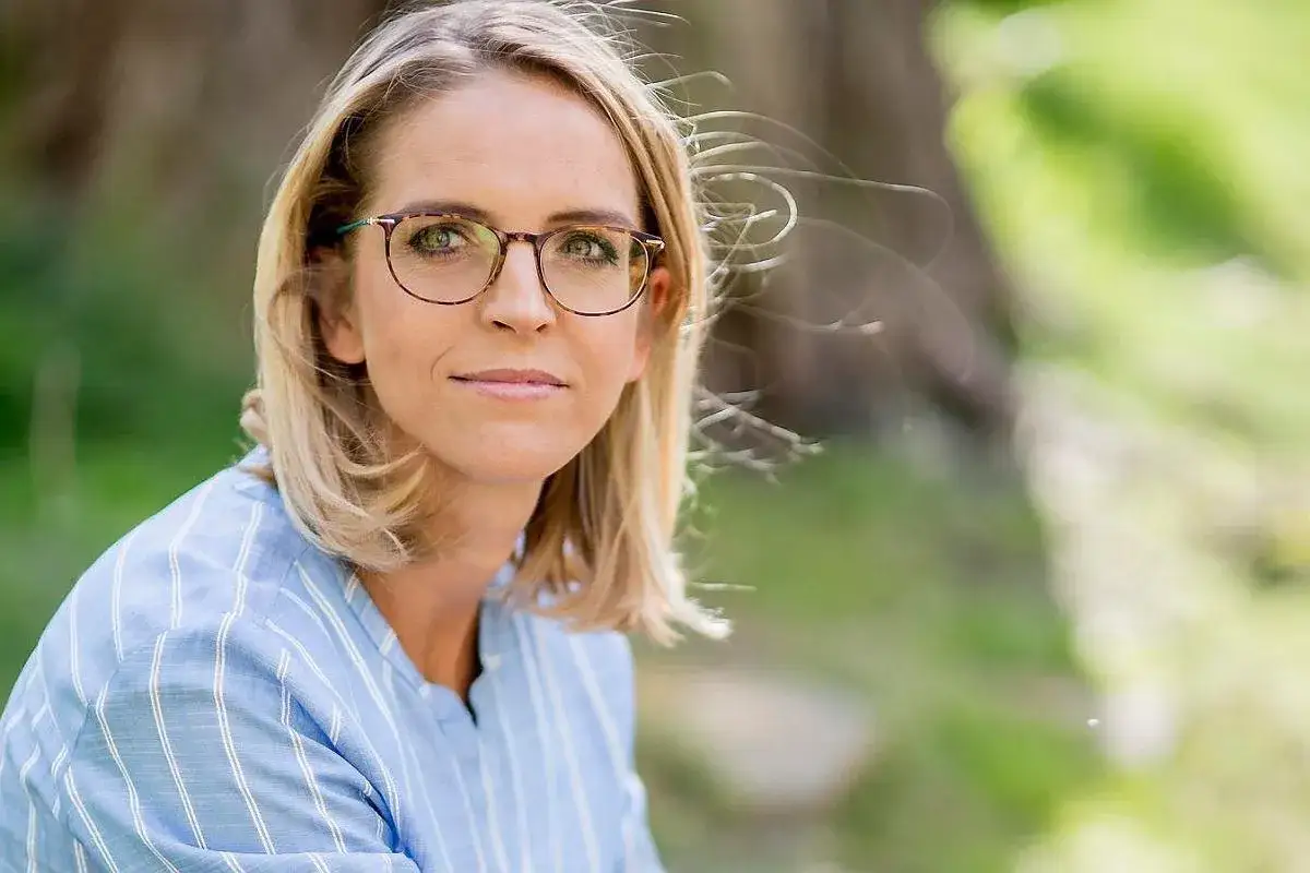 Małgorzata Trzaskowska w okularach, w niebieskiej koszuli w paski. Jej wykształcenie jest ważnym elementem jej drogi zawodowej.