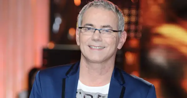 Robert Janowski ile ma lat? Uśmiechnięty mężczyzna w okularach, w granatowej marynarce i białej koszulce.